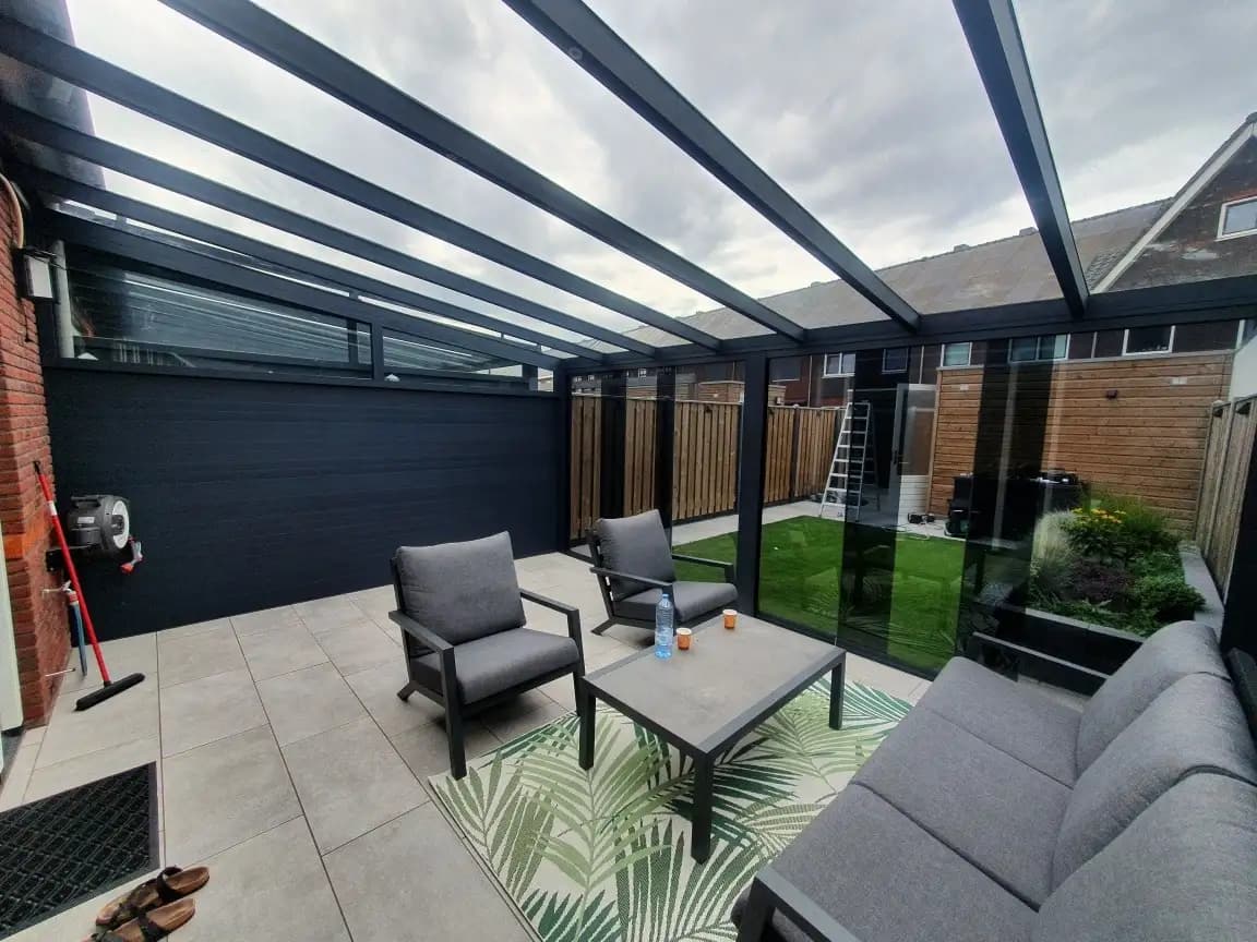 Loungeset onder een veranda met een antraciet zijwand en glazen schuifwanden naar de tuin